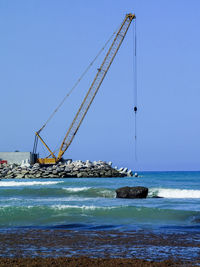 Heavy metallic machine moving rocks on the ocean in order to create a wall for the new port