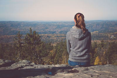 Rear view of woman sitting on a rock looking at view