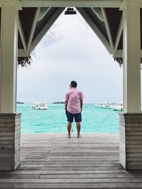 Rear view of mature man standing on pier over sea against sky