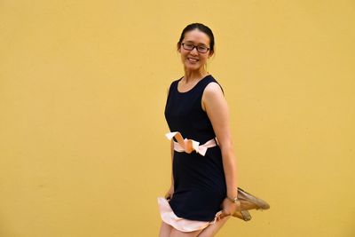 Portrait of smiling young woman against yellow background