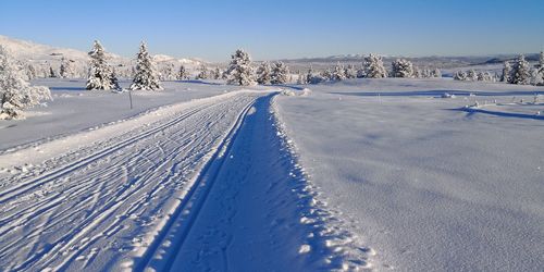 Ski tracks on snow covered landscape against blue sky