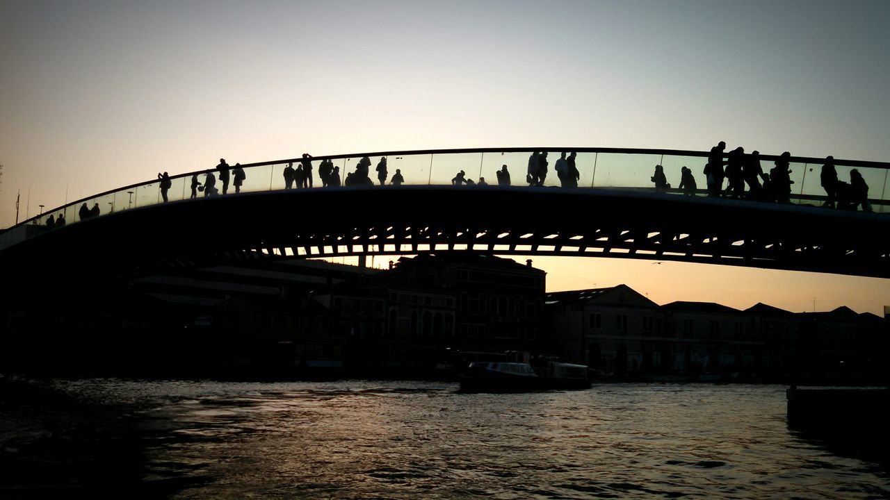 water, built structure, clear sky, architecture, bridge - man made structure, connection, transportation, silhouette, men, copy space, large group of people, bridge, river, person, lifestyles, leisure activity, medium group of people, waterfront, incidental people