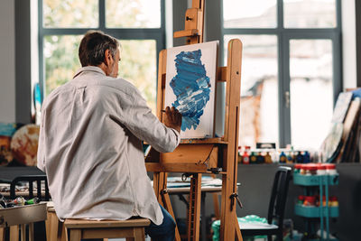Senior man with paintbrush painting at workshop
