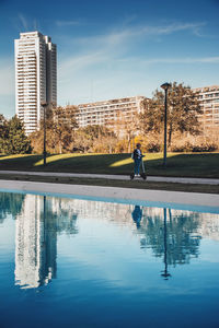 Reflection of man in swimming pool by lake against buildings in city