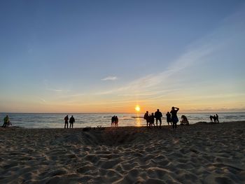 People on beach against sky during sunset