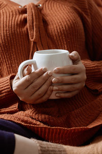 Autumn mood. young female in orange woolen pullover drinking refreshing coffee in a cold autumnal