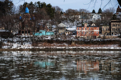 Buildings by lake in city during winter