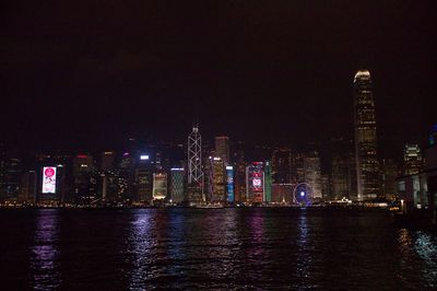 Illuminated buildings by river against sky at night