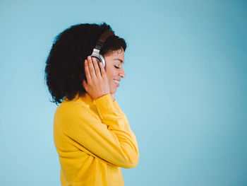Profile view of woman enjoying music on headphones against blue background