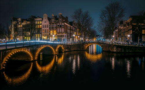 Illuminated bridge over river in city at night