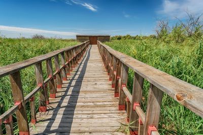 Wooden footbridge on field against sky