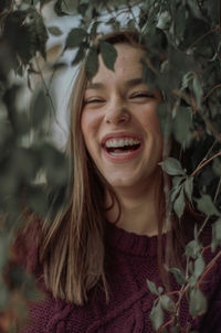 Close-up of young woman laughing while looking through plants 