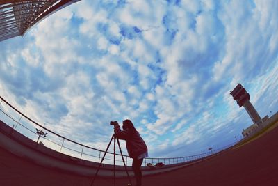 Fish-eye view of woman photographing while standing against sky