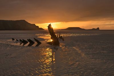 Silhouette shipwreck on beach against sky during sunset