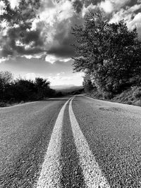 Empty road amidst trees on field against sky