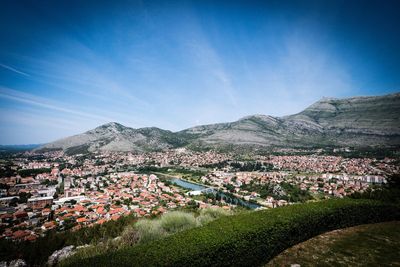 Aerial view of townscape and mountains against blue sky