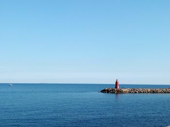 Lighthouse by sea against clear blue sky