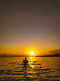 Silhouette man in sea against sky during sunset