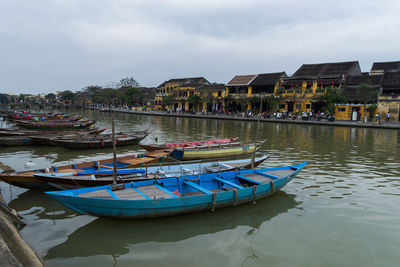 Boats moored in lake by buildings against sky