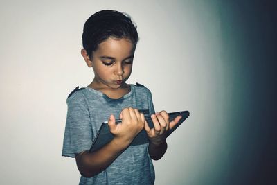 Boy holding digital tablet while standing against wall