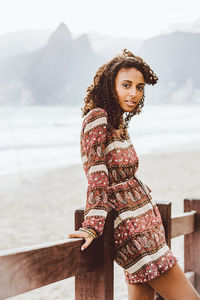 Side view portrait of young woman leaning on railing at beach