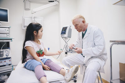 Mature doctor talking with girl while preparing pulse oxymeter at hospital