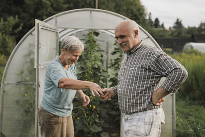 Smiling senior couple in front of green house