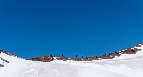 Hikers climbing mountain against clear sky