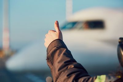 Cropped image of man gesturing against airplane at airport runway