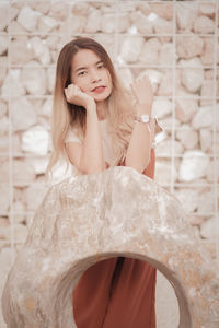Portrait of smiling young woman standing against wall