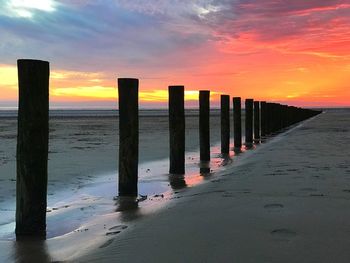 Wooden posts on beach against sky during sunset