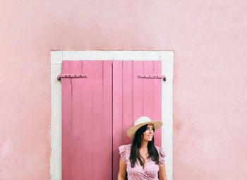 Portrait of woman standing against pink wall