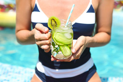 Midsection of woman holding drink in swimming pool