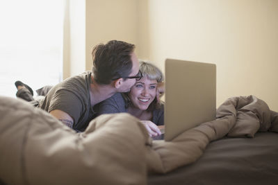 Young couple lying in bed looking at a laptop