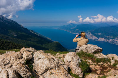 Side view of woman sitting on rock against sky