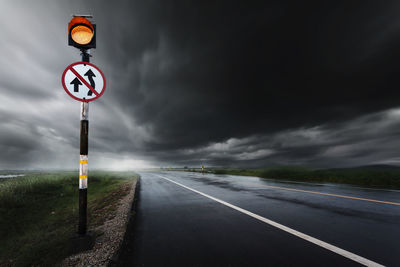 Road sign by wet road against sky