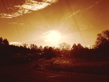 Silhouette trees on road against sky during sunset