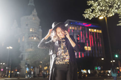 Smiling young woman answering smart phone in city at night