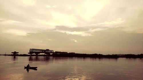 Silhouette boat in river against sky at sunset
