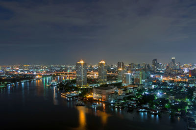 Illuminated buildings by river against sky in city at night