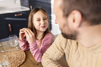 Smiling girl having breakfast with father sitting at table