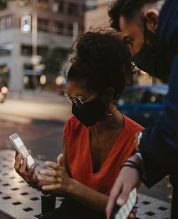 Female entrepreneur using smart phone with male colleague in city during pandemic