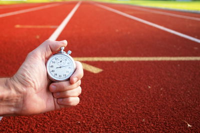 Cropped image of hand holding stopwatch against running tracks