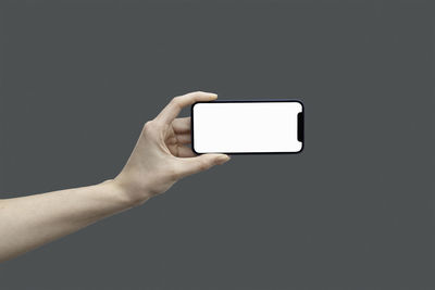 Cropped hand of person using smart phone against black background