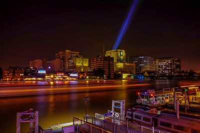 Illuminated buildings by river against sky at night