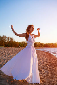 Beautiful slender woman in a white dress by the sea at sunset