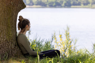 Side view of woman sitting on rock by sea