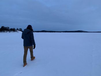 Rear view of woman standing in snow against sky