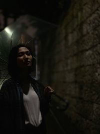 Young man looking away while standing in the dark