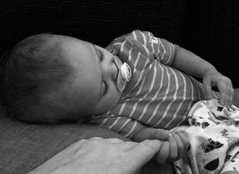 Baby sleeping while holding parent finger at home